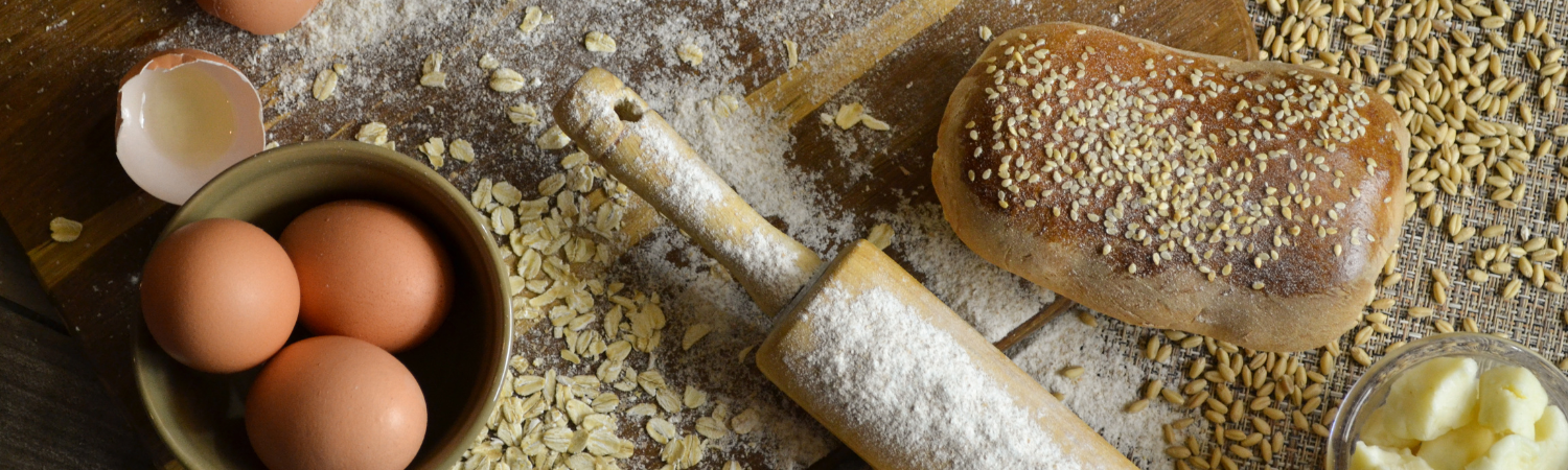 Eine Schale mit Eiern, ein Brot und ein Nudelholz liegen auf einem bemehlten Untergrund
