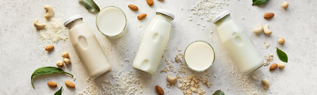 Drei Glasflaschen mit Milch gefüllt, liegend auf einer weißen Fläche mit Nüssen