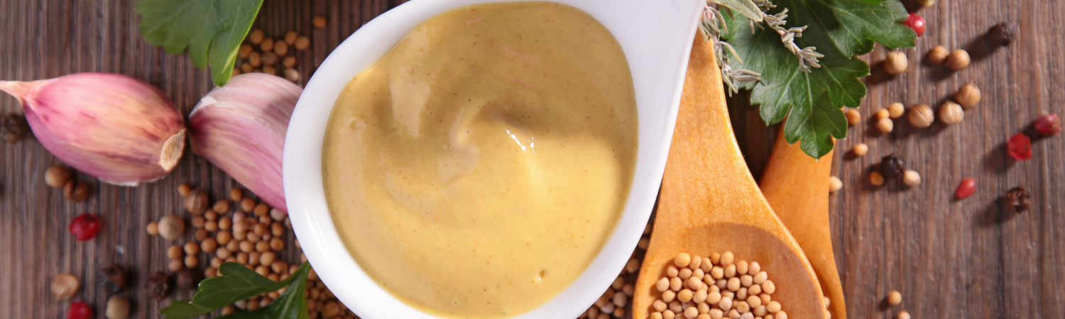Mehrere Gewürze und Knoblauch und darüber ein weißer Löffel mit Senf