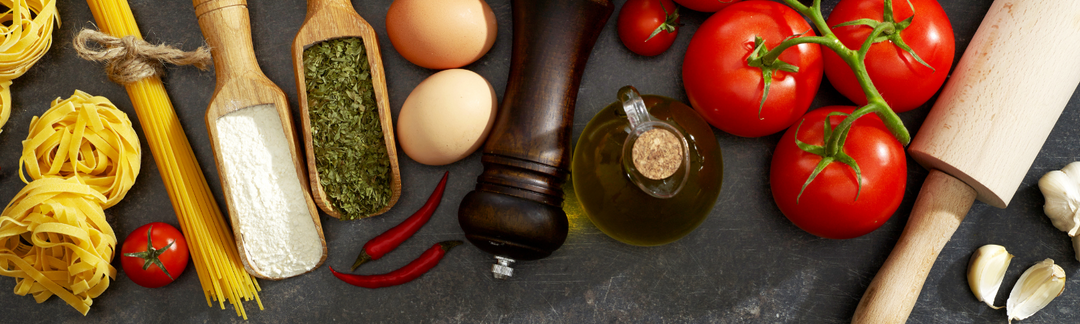 Kochzutaten wie Tomaten, Nudeln und Gewürze auf dunklem Untergrund