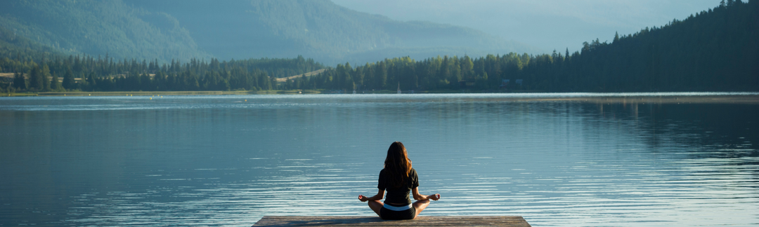 Frau macht eine Yoga Pose auf einem Holzsteg bei einem blauen See mit Bergen im Hintergrund